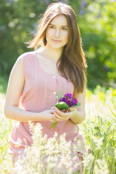 Retrato de uma bela jovem com cabelo castanho em vestido xadrez retro. Menina posando na natureza com um pequeno buquê de violetas — Fotografia de Stock