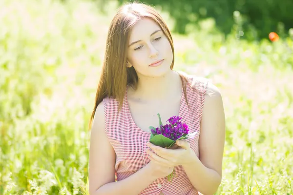 Portrait of a beautiful young woman with brown hair in retro plaid dress. Girl posing in nature with a small bouquet of violets — Stock Photo, Image