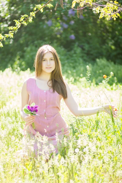 Portrait of a beautiful young woman with brown hair in retro plaid dress. Girl posing in nature with a small bouquet of violets — Stock Photo, Image