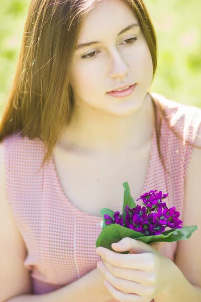 Portrait of a beautiful young woman with brown hair in retro plaid dress. Girl posing in nature with a small bouquet of violets — Stock Photo, Image