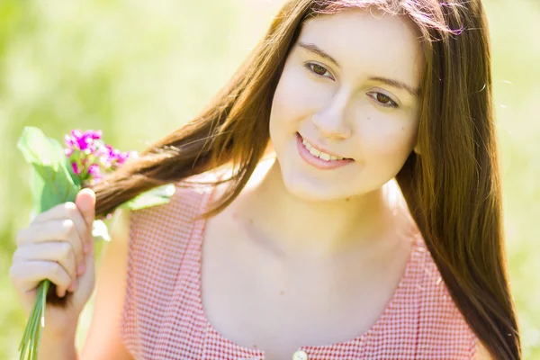 Retrato de uma bela jovem com cabelo castanho em vestido xadrez retro. Menina posando na natureza com um pequeno buquê de violetas — Fotografia de Stock