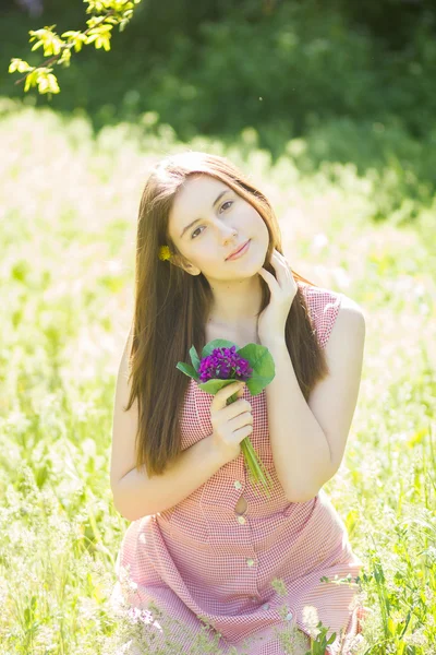 Portrait of a beautiful young woman with brown hair in retro plaid dress. Girl posing in nature with a small bouquet of violets — Stock Photo, Image