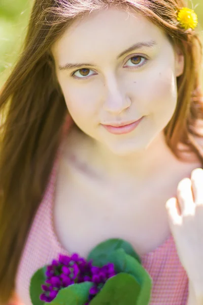 Retrato de una hermosa mujer joven con cabello castaño en vestido retro a cuadros. Chica posando en la naturaleza con un pequeño ramo de violetas — Foto de Stock