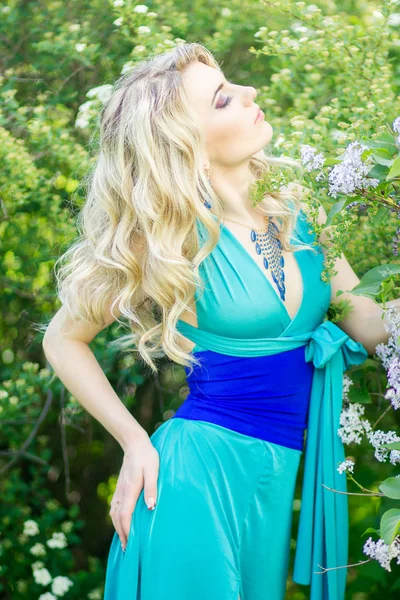 Retrato de una hermosa mujer rubia joven con el pelo largo en un vestido azul largo con una hendidura alta en la naturaleza . — Foto de Stock