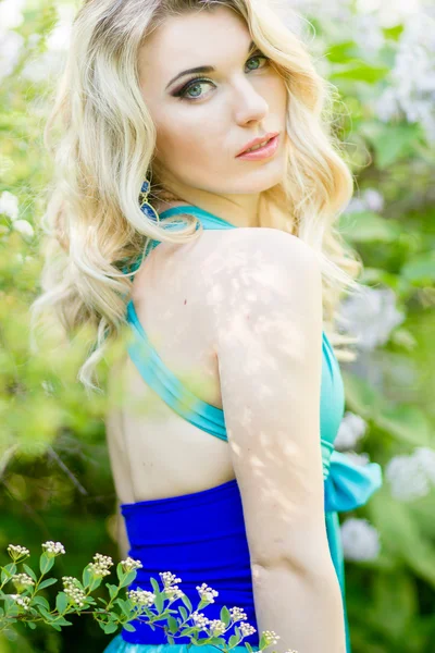 Porträt einer schönen jungen blonden Frau mit langen Haaren in einem langen blauen Kleid mit hohem Schlitz in der Natur. — Stockfoto