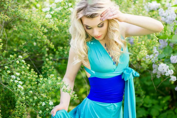 Retrato de uma bela jovem loira com cabelos longos em um longo vestido azul com uma alta fenda na natureza . — Fotografia de Stock