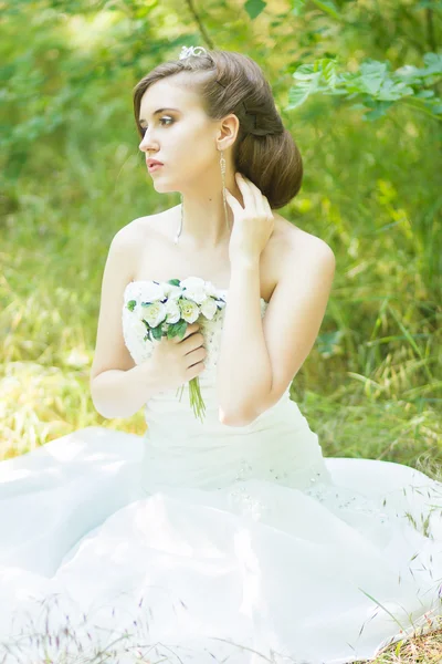 Ritratto di una bella giovane sposa in natura. Giovane donna che tiene un piccolo mazzo di rose bianche nelle loro mani — Foto Stock