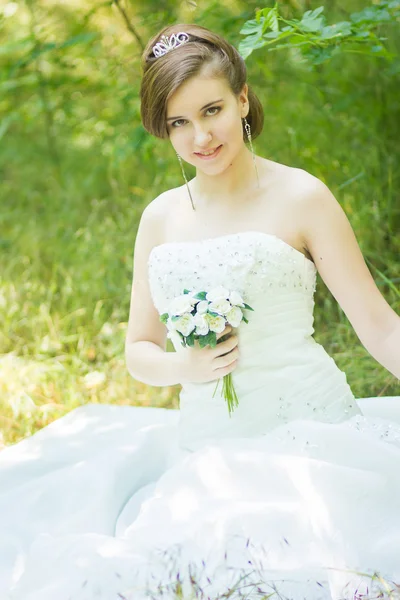 Ritratto di una bella giovane sposa in natura. Giovane donna che tiene un piccolo mazzo di rose bianche nelle loro mani — Foto Stock