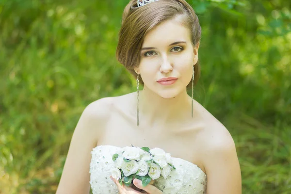 Portrait of a beautiful young bride in nature. Young woman holding a small bouquet of white roses in their hands — Stock Photo, Image