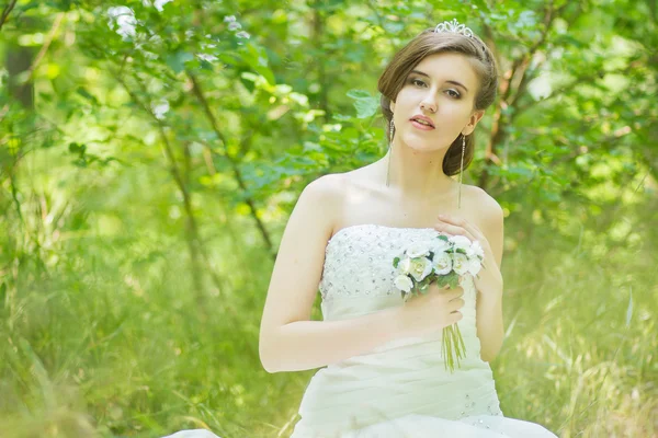 Ritratto di una bella giovane sposa in natura. Giovane donna che tiene un piccolo mazzo di rose bianche nelle loro mani — Foto Stock