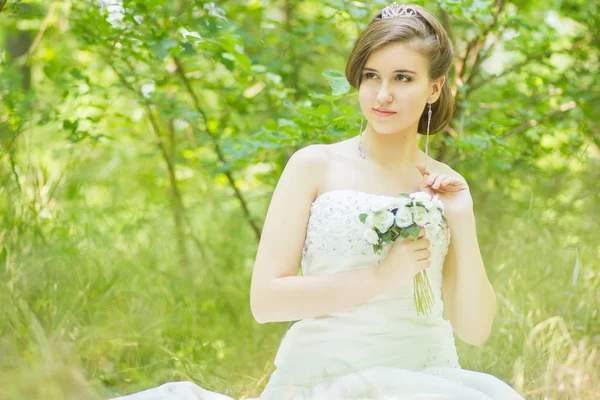 Ritratto di una bella giovane sposa in natura. Giovane donna che tiene un piccolo mazzo di rose bianche nelle loro mani — Foto Stock