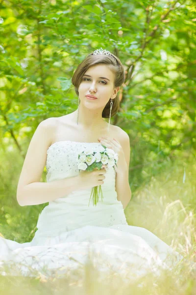 Portrait of a beautiful young bride in nature. Young woman holding a small bouquet of white roses in their hands — Stock Photo, Image
