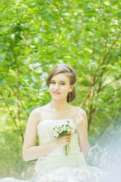 Porträtt av en vacker ung brud i naturen. ung kvinna med en liten bukett vita rosor i händerna — Stockfoto