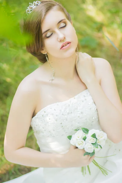 Portret van een mooie jonge bruid in de natuur. jonge vrouw met een kleine boeket van witte rozen in hun handen — Stockfoto