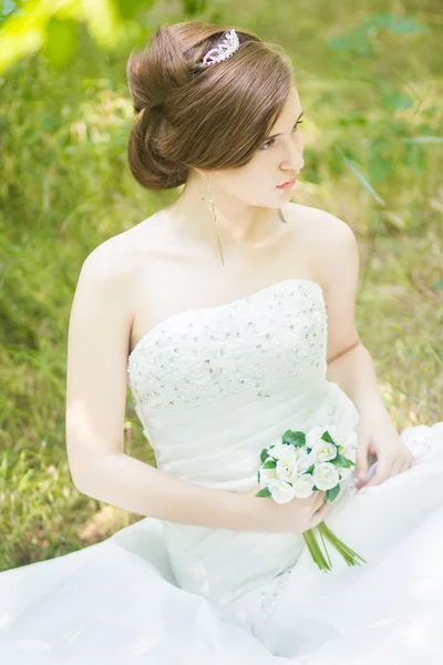 Porträt einer schönen jungen Braut in der Natur. junge Frau mit einem kleinen Strauß weißer Rosen in der Hand — Stockfoto