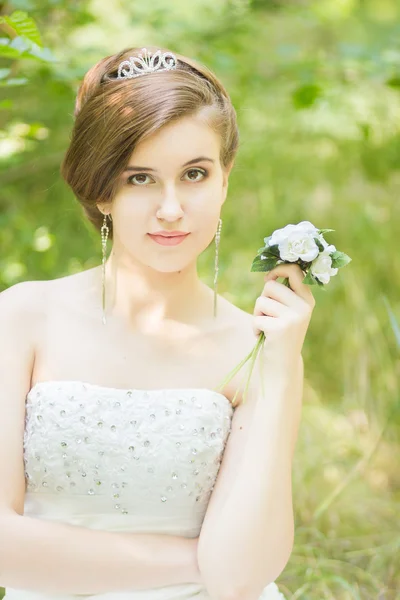 Porträt einer schönen jungen Braut in der Natur. junge Frau mit einem kleinen Strauß weißer Rosen in der Hand — Stockfoto