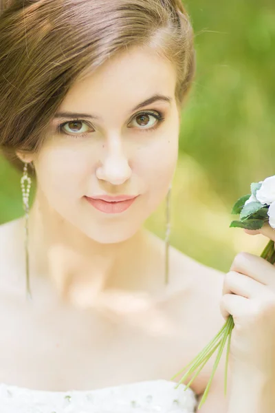 Retrato de uma bela noiva jovem na natureza. Jovem segurando um pequeno buquê de rosas brancas em suas mãos — Fotografia de Stock