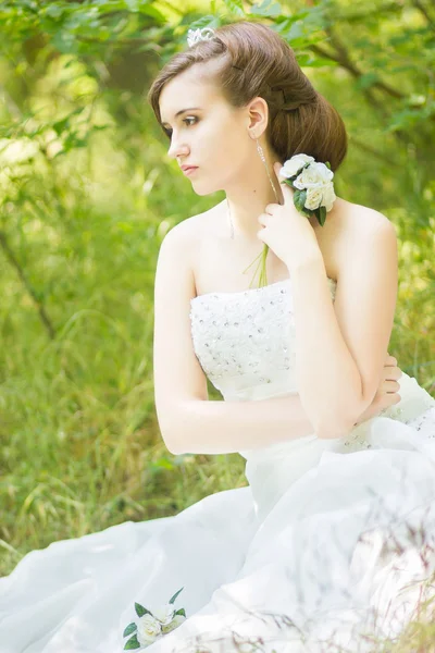 Портрет красивой молодой невесты на природе. Молодая женщина держит в руках маленький букет белых роз — стоковое фото