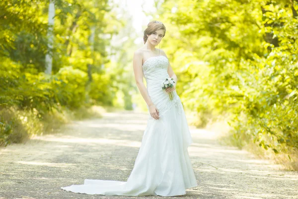 Retrato de uma bela noiva jovem na natureza. Jovem segurando um pequeno buquê de rosas brancas em suas mãos — Fotografia de Stock