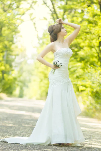 Portrait of a beautiful young bride in nature. Young woman holding a small bouquet of white roses in her hands — Stock Photo, Image