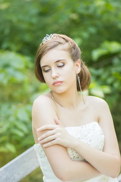 Portrait of a beautiful young bride in nature. Girl sitting on a park bench. — Stock Photo, Image