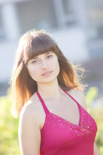 Portrait of a beautiful young woman with brown hair in red light dress. Girl in the garden with rose bushes — Stock Photo, Image