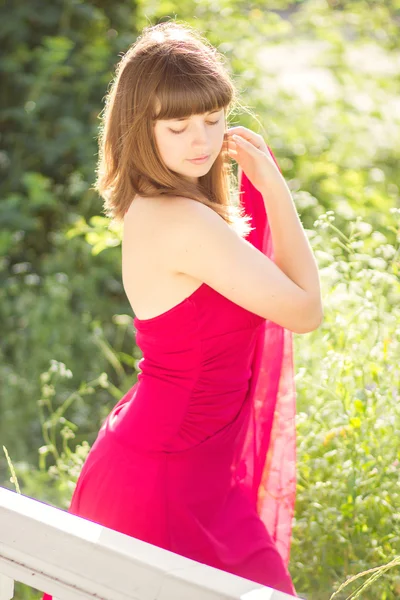 Retrato de una hermosa joven con cabello castaño en vestido rojo claro. Chica en el jardín con rosales —  Fotos de Stock