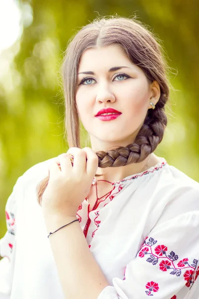 Outdoor fashion brown hair woman portrait in embroidered Ukrainian national costume. Beautiful woman with bright makeup posing on the nature — Stock Photo, Image