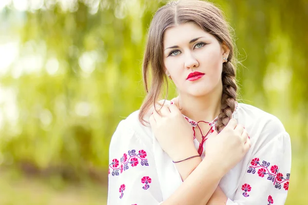 Outdoor fashion brown hair woman portrait in embroidered Ukrainian national costume. Beautiful woman with bright makeup posing on the nature — Stock Photo, Image