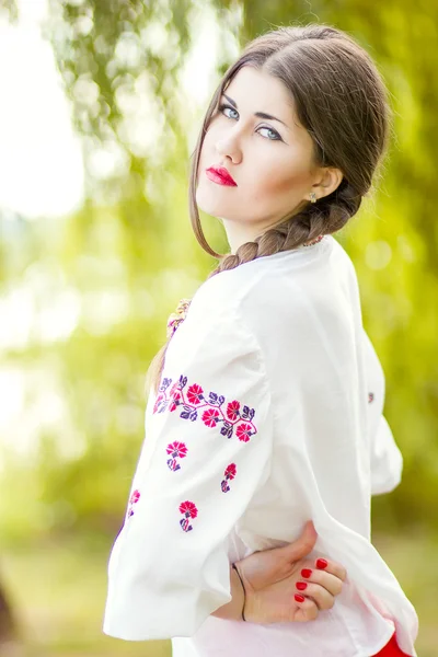 Outdoor fashion brown hair woman portrait in embroidered Ukrainian national costume. Beautiful woman with bright makeup posing on the nature — Stock Photo, Image