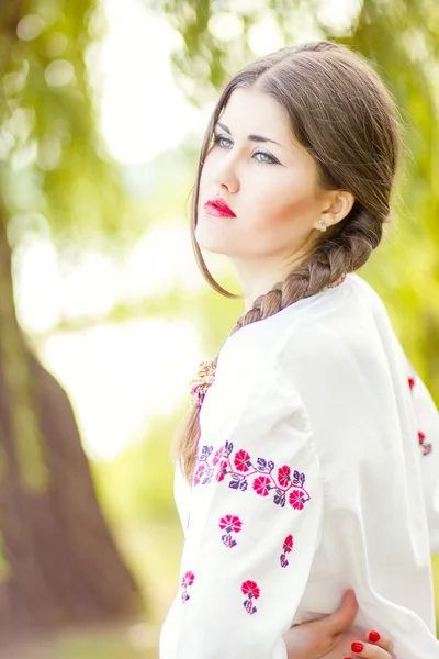 Outdoor fashion brown hair woman portrait in embroidered Ukrainian national costume. Beautiful woman with bright makeup posing on the nature — Stock Photo, Image
