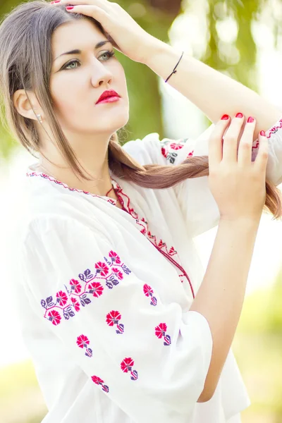 Retrato de mujer de pelo castaño de moda al aire libre en traje nacional ucraniano bordado. Hermosa mujer con maquillaje brillante posando sobre la naturaleza — Foto de Stock