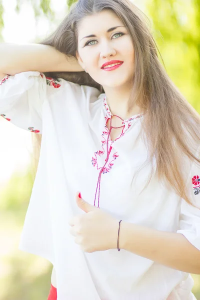 Outdoor fashion brown hair woman portrait in embroidered Ukrainian national costume. Beautiful woman with bright makeup posing on the nature — Stock Photo, Image