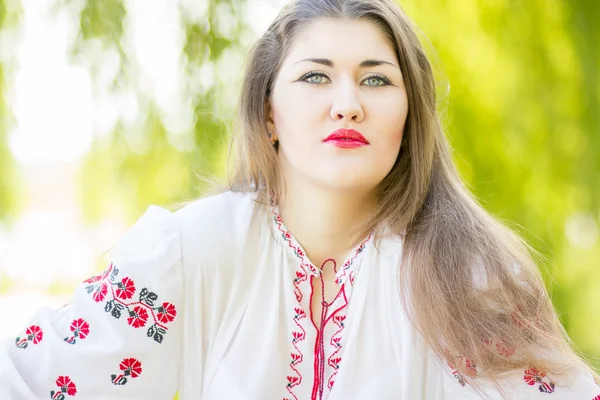 Outdoor fashion brown hair woman portrait in embroidered Ukrainian national costume. Beautiful woman with bright makeup posing on the nature — Stock Photo, Image