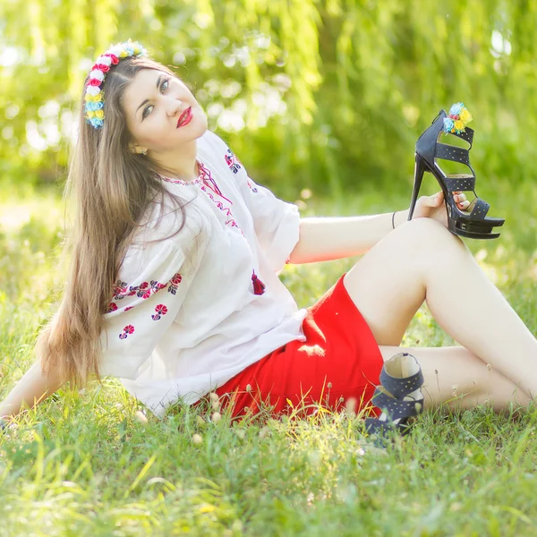 Outdoor portrait young woman with long brown hair. The girl floral accessories, she poses lying on the grass in the park — Stock Photo, Image