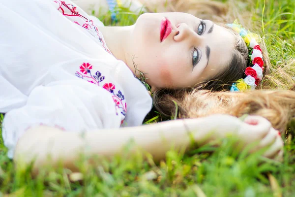 Внешний портрет молодой женщины с длинными каштановыми волосами. Девушка цветочные аксессуары, она позирует лежа на траве в парке — стоковое фото