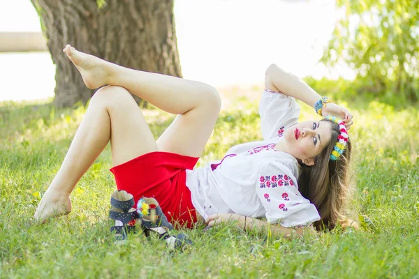 Utomhus porträtt ung kvinna med långa bruna hår. blommig tillbehören till flicka, hon ställer liggande på gräset i parken — Stockfoto