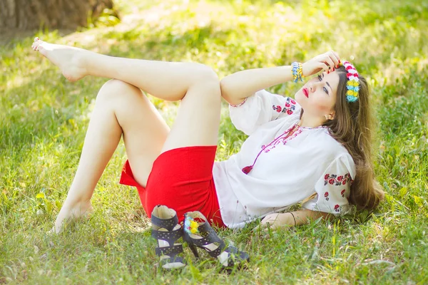 Outdoor portrait young woman with long brown hair. The girl floral accessories, she poses lying on the grass in the park — Stock Photo, Image