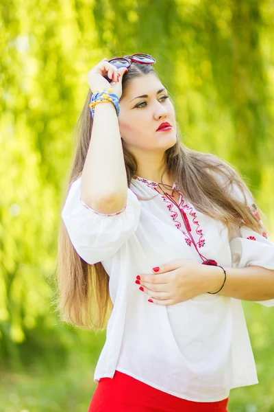 Portrait of a beautiful young woman with long brown hair who poses with sunglasses. The girl is on the nature and smiling. — Stock Photo, Image