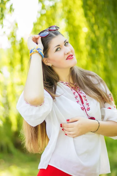 Retrato de uma bela jovem com cabelos castanhos longos que posa com óculos de sol. A menina está na natureza e sorrindo . — Fotografia de Stock