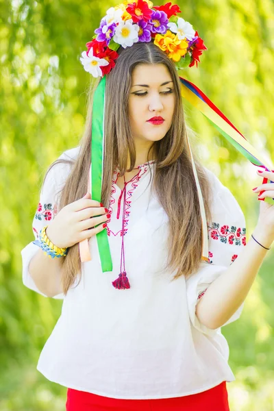 Portrait d'une belle jeune femme aux longs cheveux bruns dans la nature en chemisier. Fille posant avec une couronne de fleurs colorées. Concentration douce . — Photo