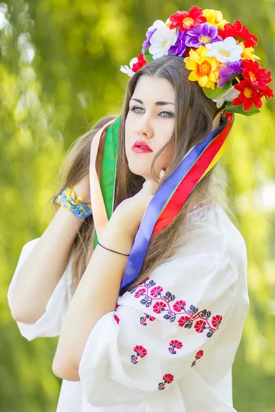 Portret to piękna młoda kobieta z długie brązowe włosy w przyrodzie w bluzka. dziewczyna pozuje z wieniec kolorowych kwiatów. nieostrość. — Zdjęcie stockowe