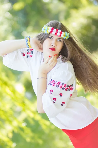 Retrato de uma bela jovem com longos cabelos castanhos na natureza em uma blusa. Menina posando com uma coroa de flores coloridas. Foco suave . — Fotografia de Stock