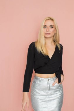 Fashion model woman in fashionable clothes on pink background. Wearing stylish clothing, black blouse, silver skirt. Posing in studio