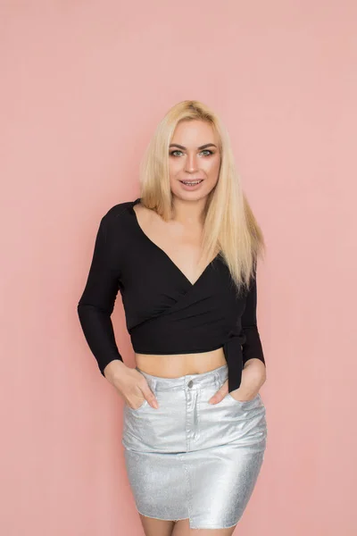 Fashion model woman in fashionable clothes on pink background. Wearing stylish clothing, black blouse, silver skirt. Posing in studio