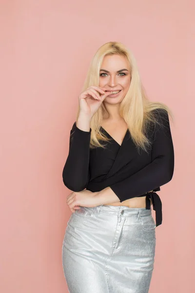 Fashion model woman in fashionable clothes on pink background. Wearing stylish clothing, black blouse, silver skirt. Posing in studio