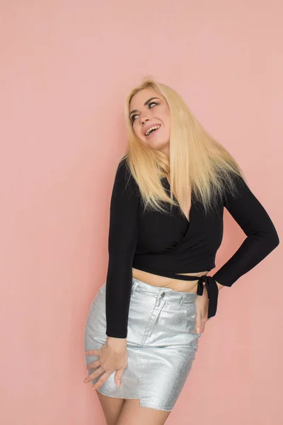 Fashion model woman in fashionable clothes on pink background. Wearing stylish clothing, black blouse, silver skirt. Posing in studio