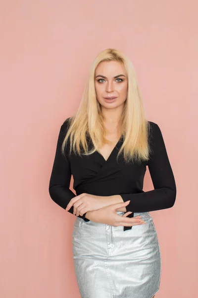 Fashion model woman in fashionable clothes on pink background. Wearing stylish clothing, black blouse, silver skirt. Posing in studio