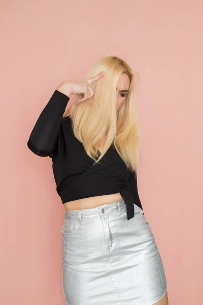 Fashion model woman in fashionable clothes on pink background. Wearing stylish clothing, black blouse, silver skirt. Posing in studio