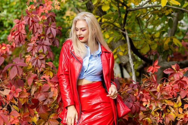秋の公園に立つ青いシャツ 赤いスカート 革のジャケットの美しいスタイリッシュな女性 可愛いです女性とともに長いですブロンドヘアスタイルと赤い唇 — ストック写真